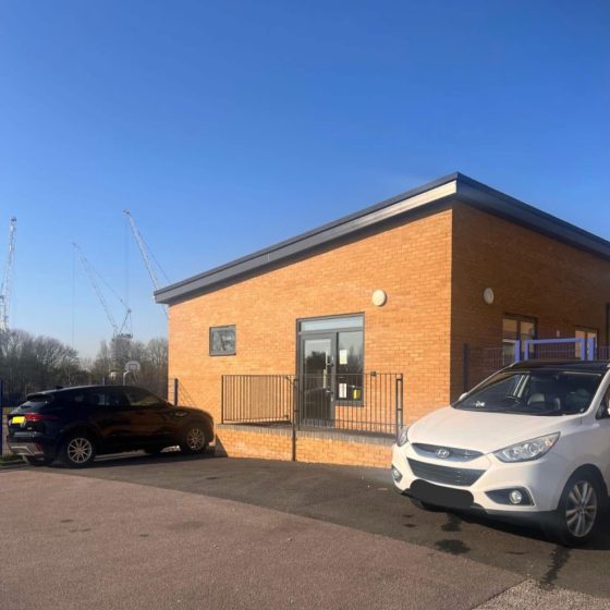 JHN Community Hub A modern brick building beside two parked cars under a clear blue sky.